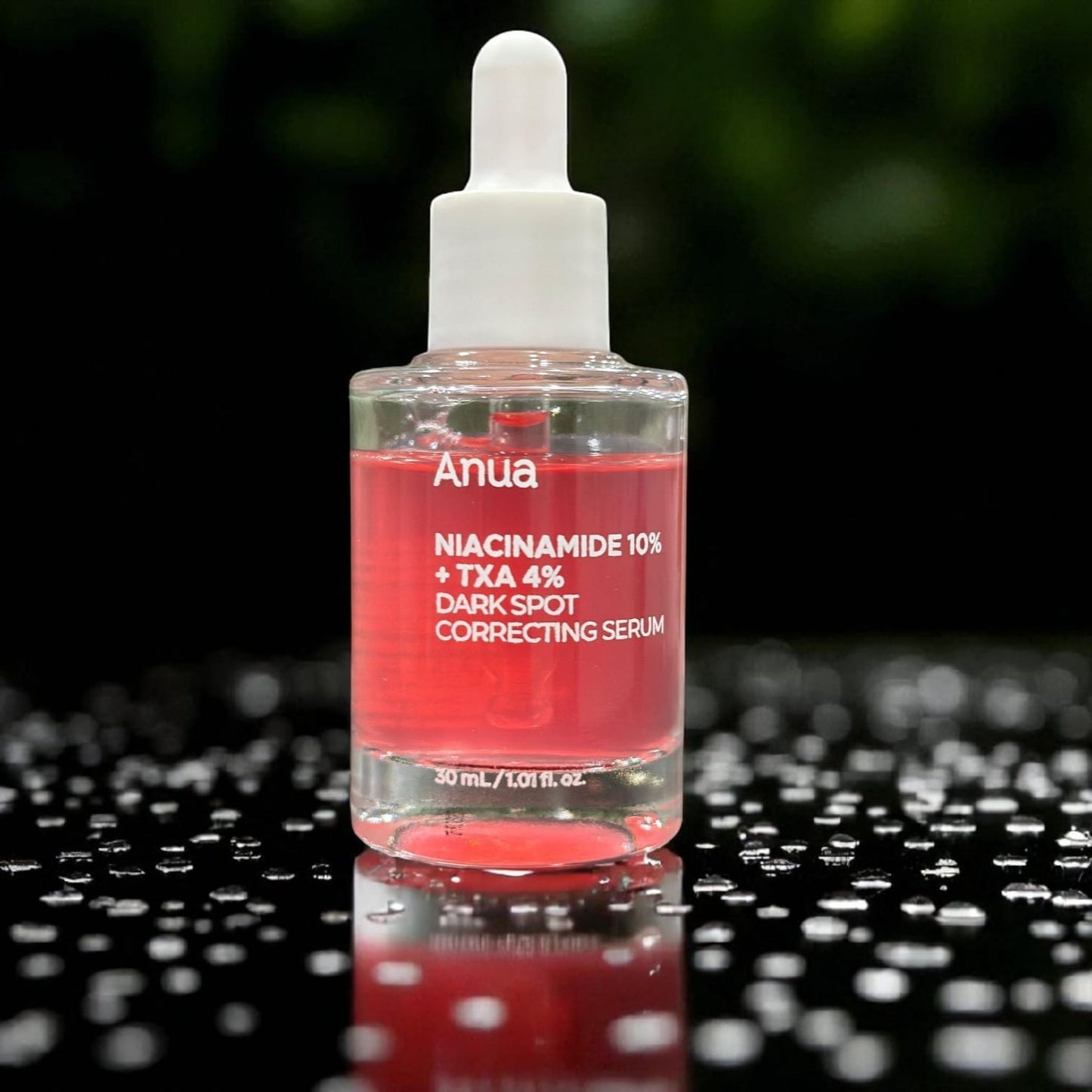 Anua dark spot correcting serum bottle with red liquid on a reflective black surface.