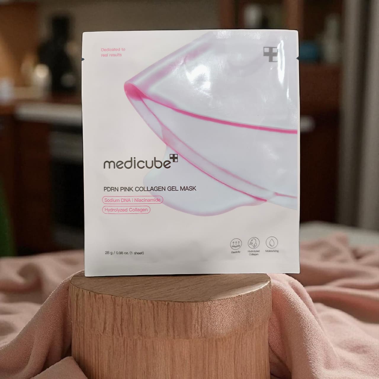 Box of Medicube pink collagen gel mask on a wooden stand with a blurred background
