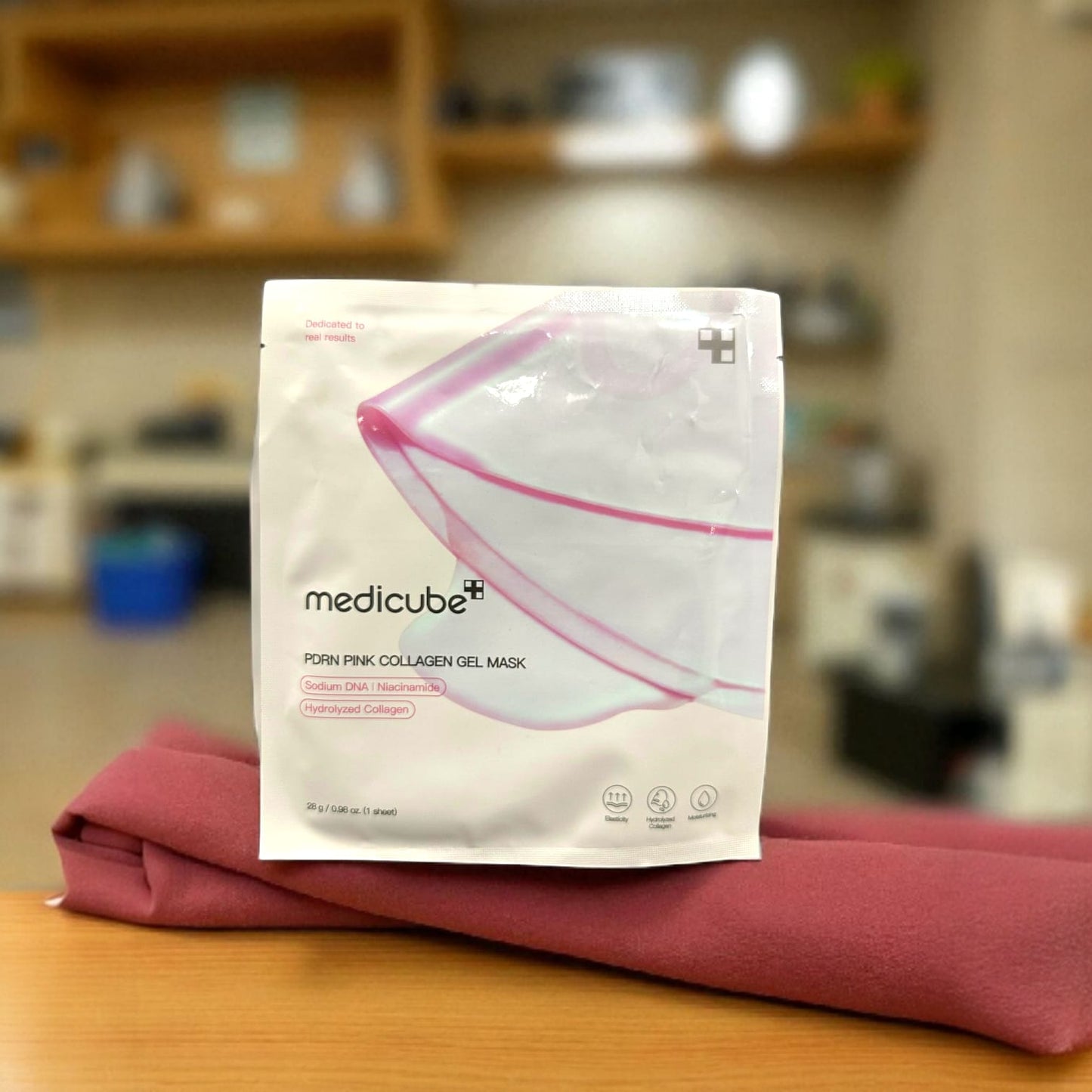 Medicube pink collagen gel mask packaging on a wooden surface with a blurred background
