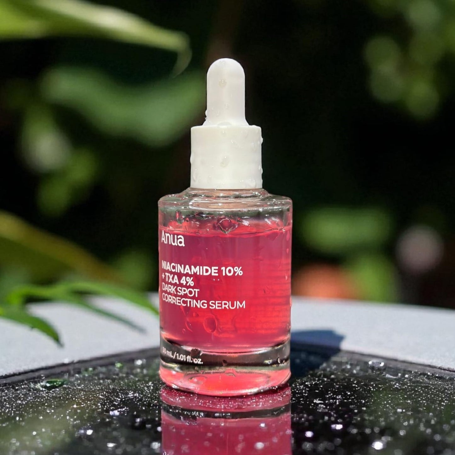 Pink serum bottle with dropper on a reflective surface outdoors